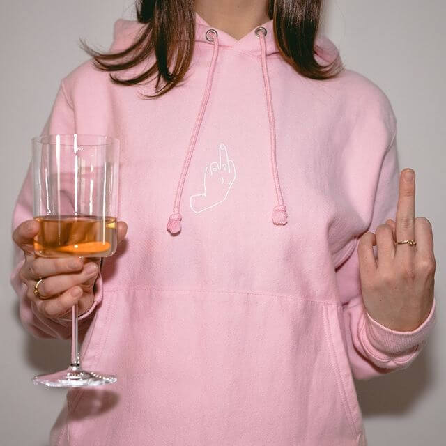 A girl wearing a FLO hoodie with a glass of wine and showing her middle finger